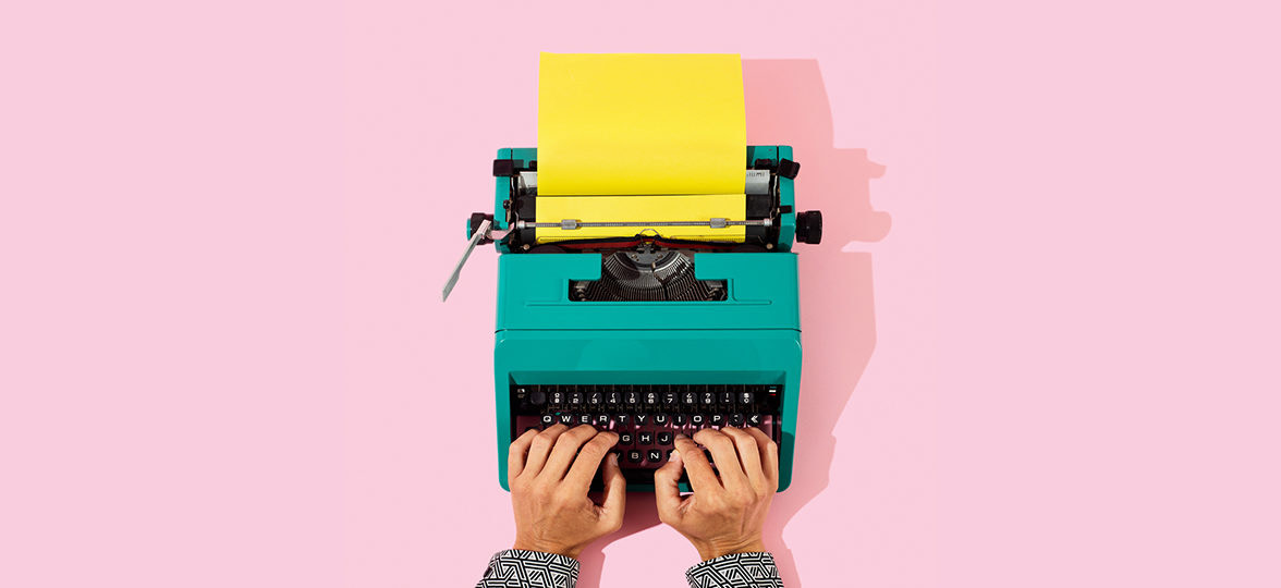 Hands typing on colorful vintage typewriter with yellow paper on pink background