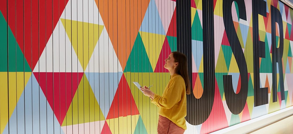 Woman looking at big colorful mural with a geometric pattern design and the word user written in big letters