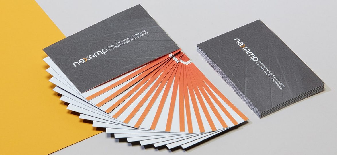 Stack of grey Nexamp business cards and Nexamp cotton business cards fanned out so we see an orange line at the bottom of the design