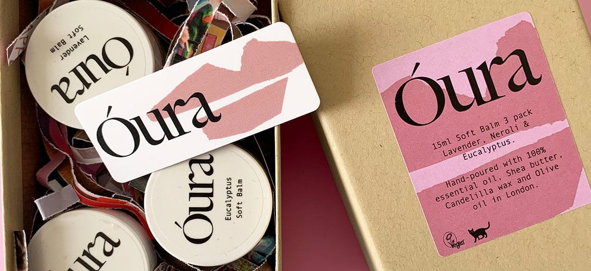 Óura's gift box with branded round stickers on balm jars, a mini card with rounded corners and a branded rectangle label to decorate the box, on a pink background