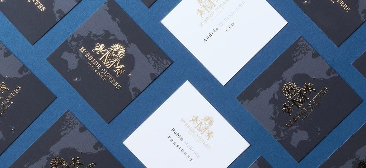 Mosaic of square black business cards with a gold foil McBride Sisters crest on the back and contact details on a white background on the front