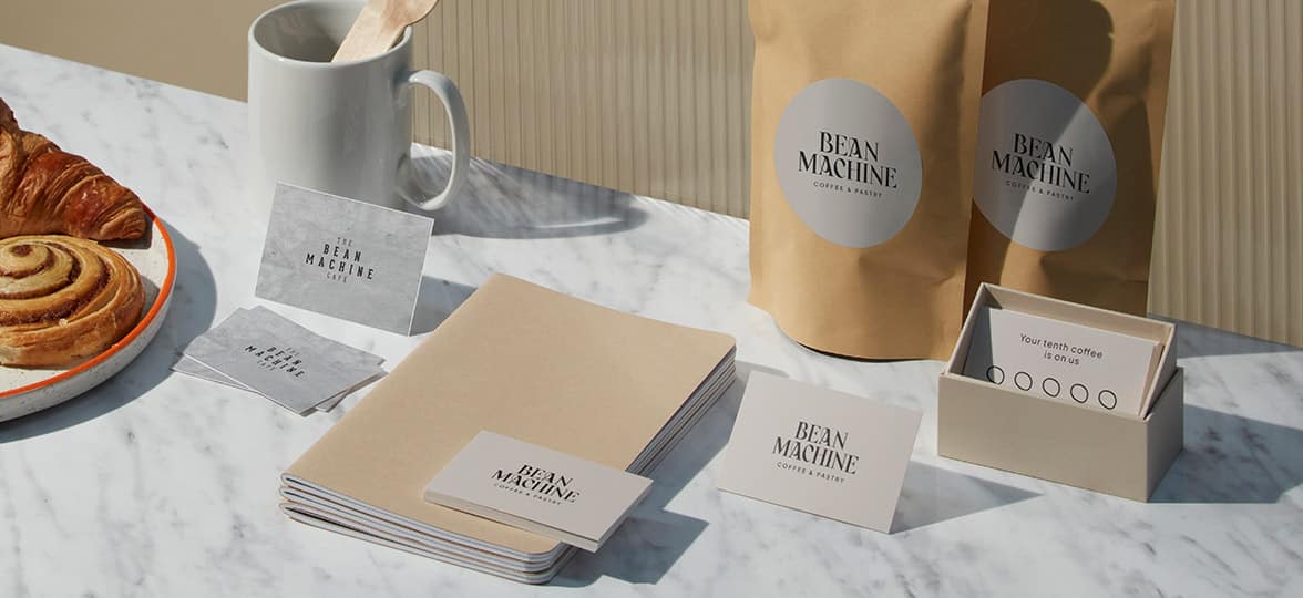 On a table next to some pastries sits business cards with two different designs, as well as bags of coffee beans with stickers that show updated branding.