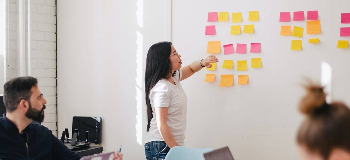 Person sticking Post-It notes to a white board in a meeting