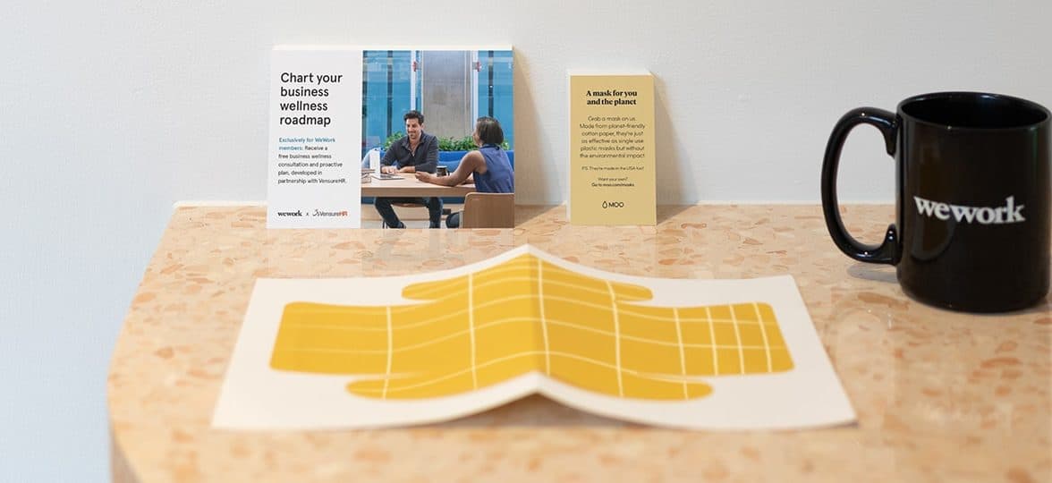 WeWork yellow paper face mask on a desk with a postcard and a business card by MOO