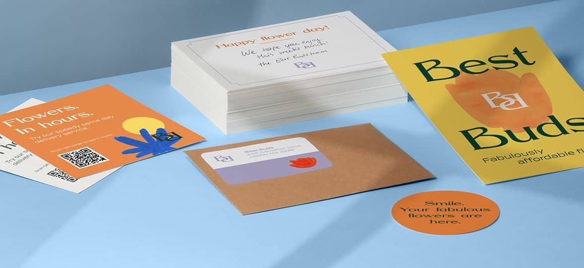 Orange and yellow flyers, postcards and round sticker next to a pile of white postcards and a brown craft envelope by fictional brand Best Buds