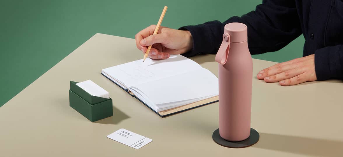 Person writing on a notrbook at their desk, with a pink water bottle