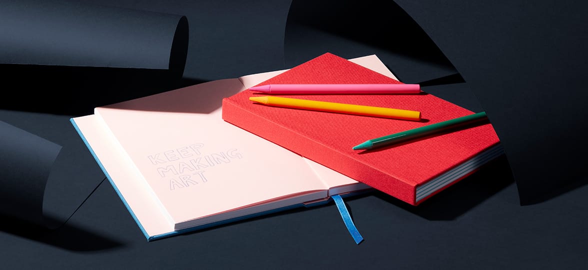 Open and closed notebooks on top of a desk with colorful pens.