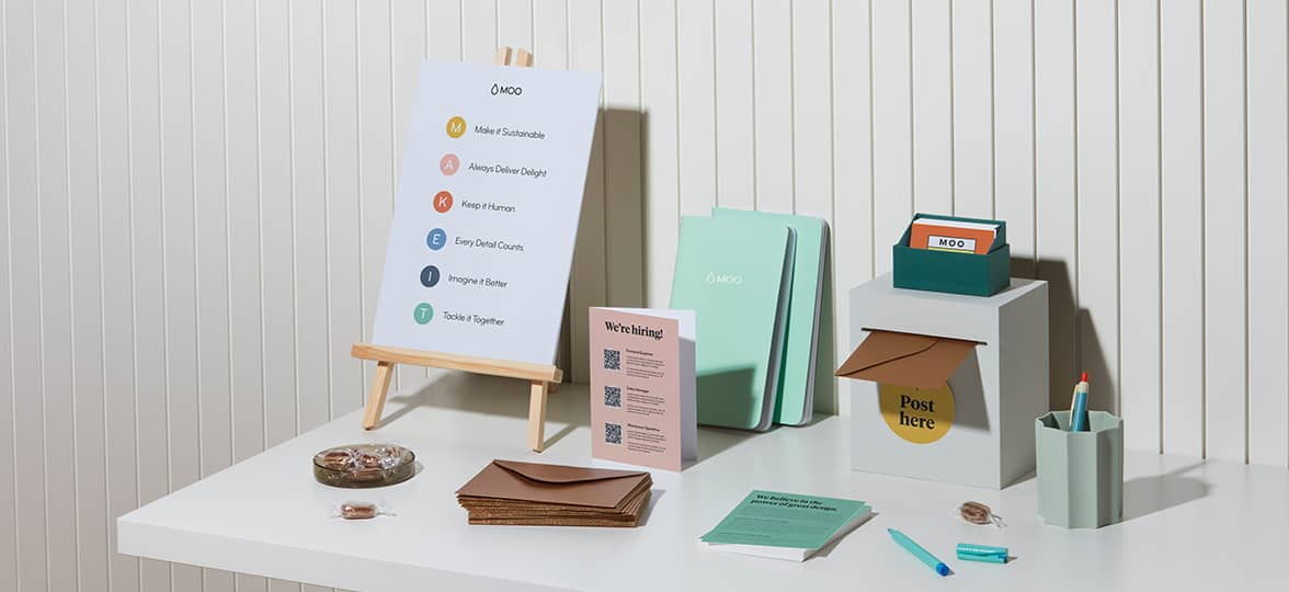 A collection of items on a display table at a recruiting fair. Branded soft-cover journals, postcards with company information, business cards, and a flyer with company values.