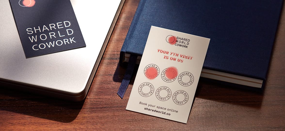 A loyalty card for a coworking space sits on a desk next to a notebook. Two of the spaces on the loyalty card have been stamped.