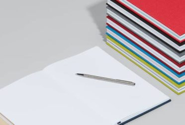 Open notebook next to a stack of hardcover notebooks with colorful cloth covers