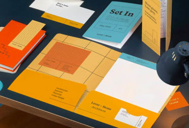 Black desk with lamp and collection of print materials in orange, blue and yellow, including greeting cards, custom notebooks, stickers, and folded flyer