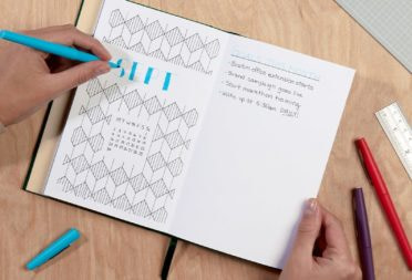 Hands drawing and writing in a dotted journal