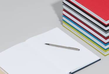 Open notebook next to a stack of hardcover notebooks with colorful cloth covers