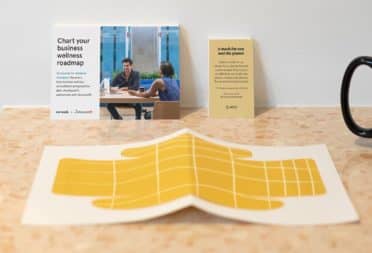 WeWork yellow paper face mask on a desk with a postcard and a business card by MOO
