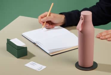 Person writing on a notrbook at their desk, with a pink water bottle