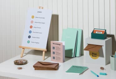 A collection of items on a display table at a recruiting fair. Branded soft-cover journals, postcards with company information, business cards, and a flyer with company values.