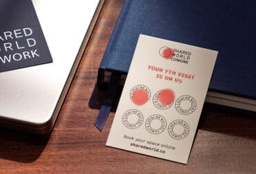 A loyalty card for a coworking space sits on a desk next to a notebook. Two of the spaces on the loyalty card have been stamped.