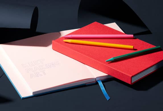 Open and closed notebooks on top of a desk with colorful pens.