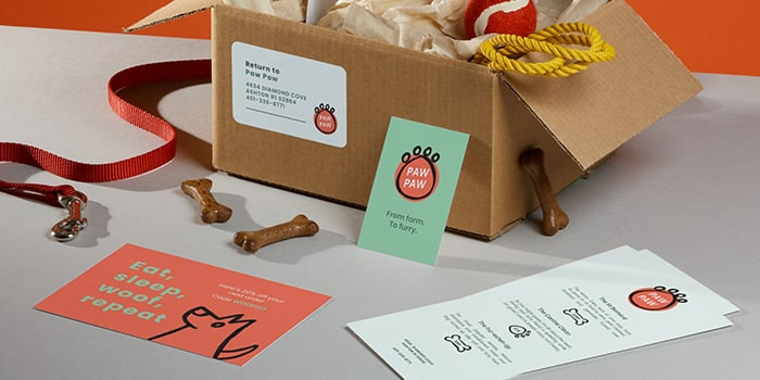 Box with dog treats, rectangular address label, green business card with a paw logo, red postcard and menu flyer for fictional brand Paw Paw