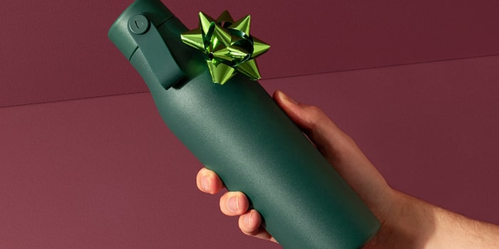 Hand holding a refillable green water bottle with a light green gift bow on it