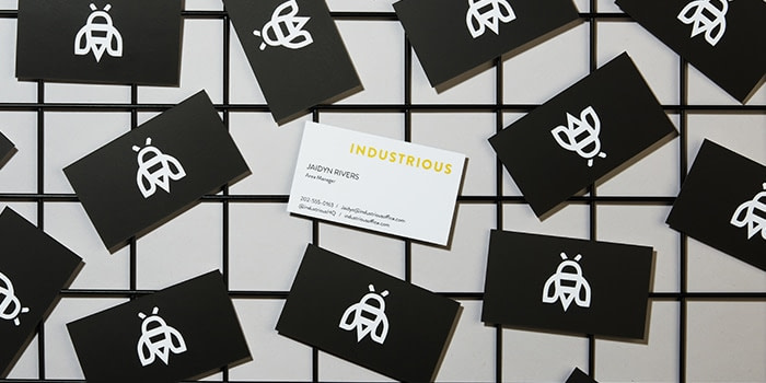 Front of an Industrious business card with contact details on a white background, surrounded by black business cards with a bee logo