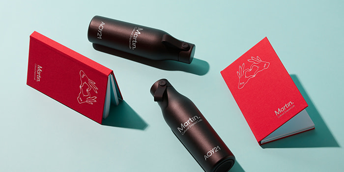 Black water bottles and red notebooks by Martin Agency and MOO