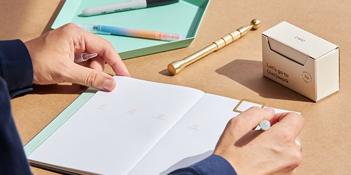 Person at their desk writing in a MOO planner open to the weekly spread