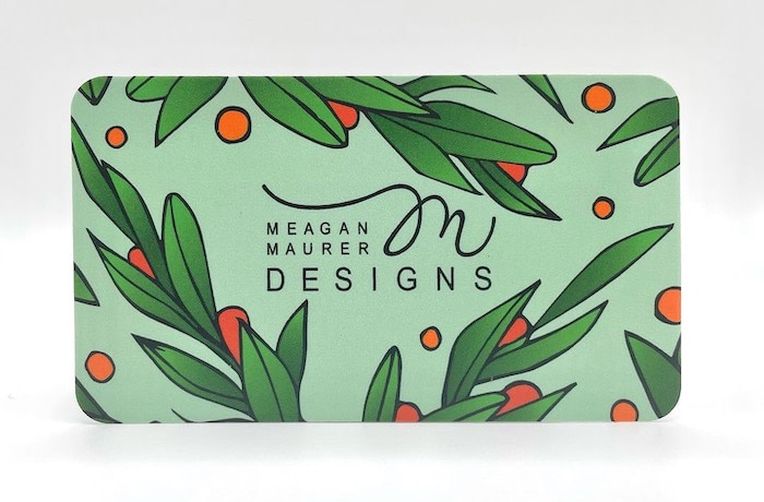 Meagan Maurer business card with rounded corners. The card is green with illustrated leaves and berries