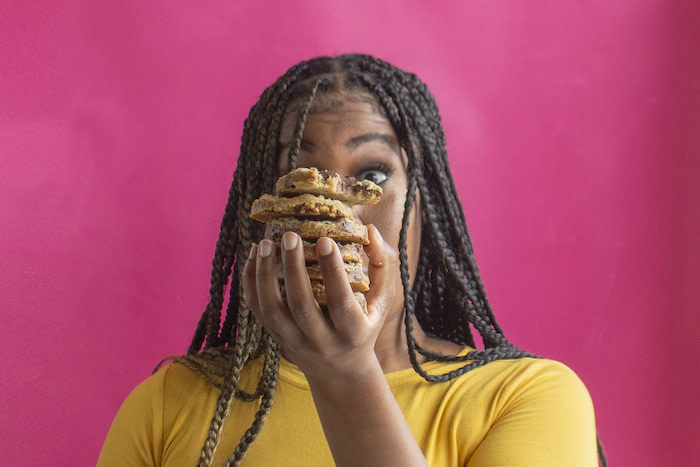 Dluxe Sweets founder Alexis Sanders holding a pile of cookies in front of her face