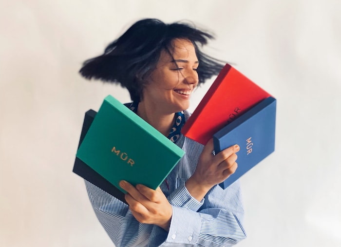 Ayca Kilicoglu, founder of Mur by Ayca, holding brand boxes in various colors and moving her hair
