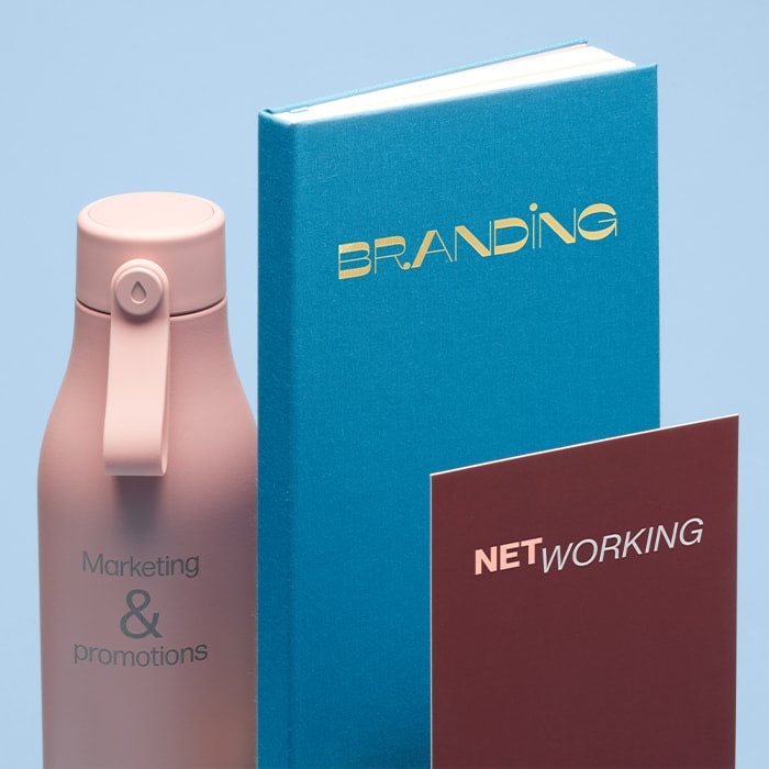 Pink water bottle with text reading marketing & promotions, blue notebook with the word branding, and postcard with the work networking