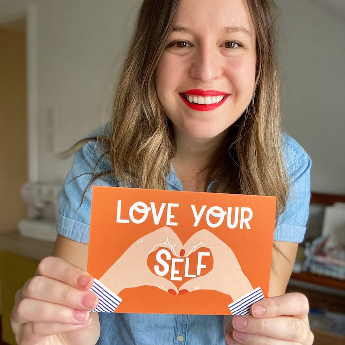 Krystal Zorzi holding a Love Yourself postcard she designed