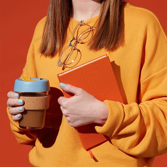 Creative woman in orange jumper improving creativity by carrying a hard cover notebook and a coffee